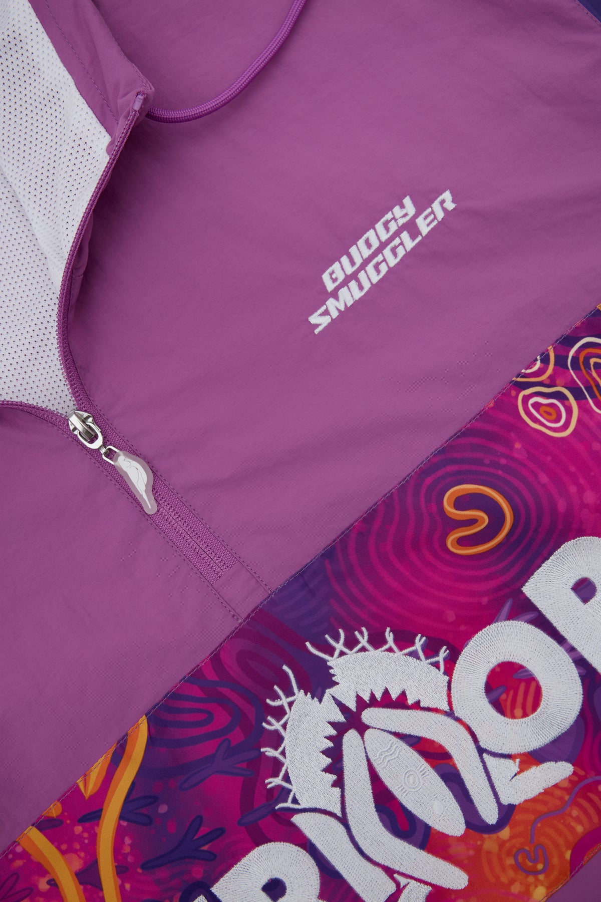 Close-up of a purple athletic zip jacket with white 'Budgy SMUGGLER' branding on the chest, shown against a colourful patterned lower section.