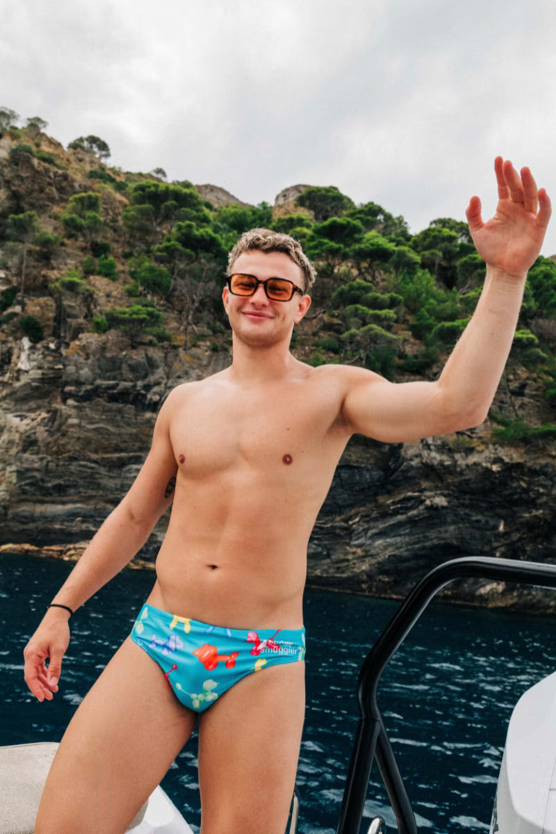Man wearing blue swimwear briefs with dogs on them by the water 