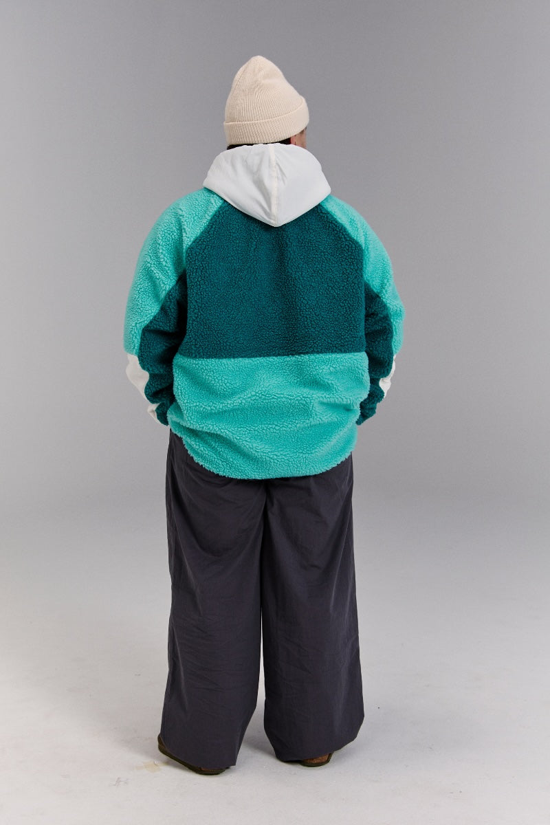 Person wearing a teal and gray striped sweater with dark pants on a plain background