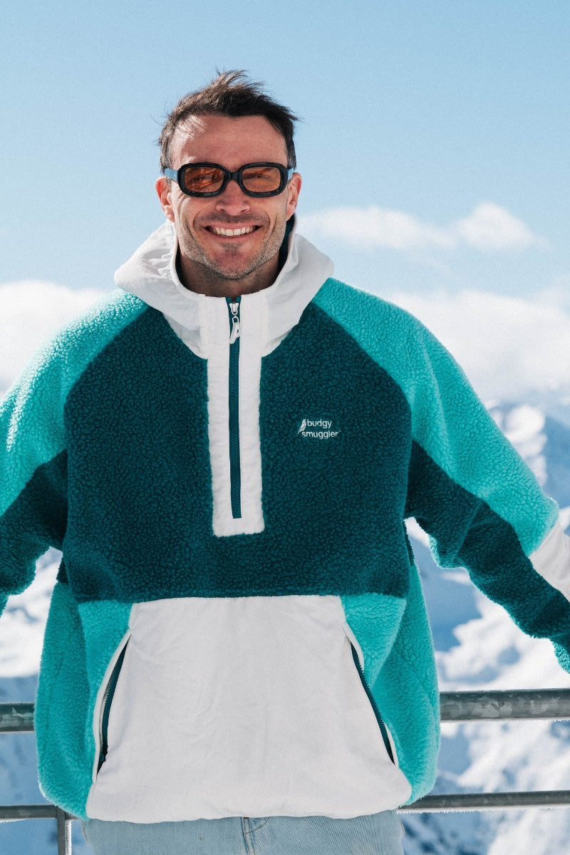 Man wearing a teal and white sweater with a logo, standing in a snowy landscape.