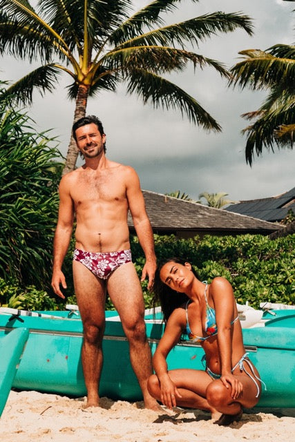 Two people in swimwear standing on a beach with palm trees in the background
