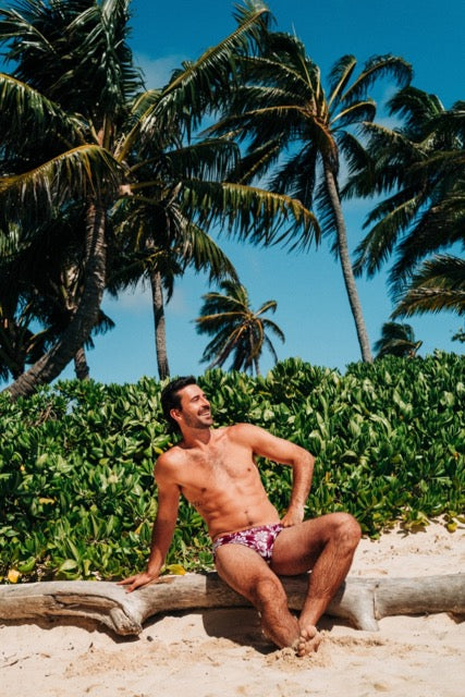 Man sitting on a log by palm trees and greenery