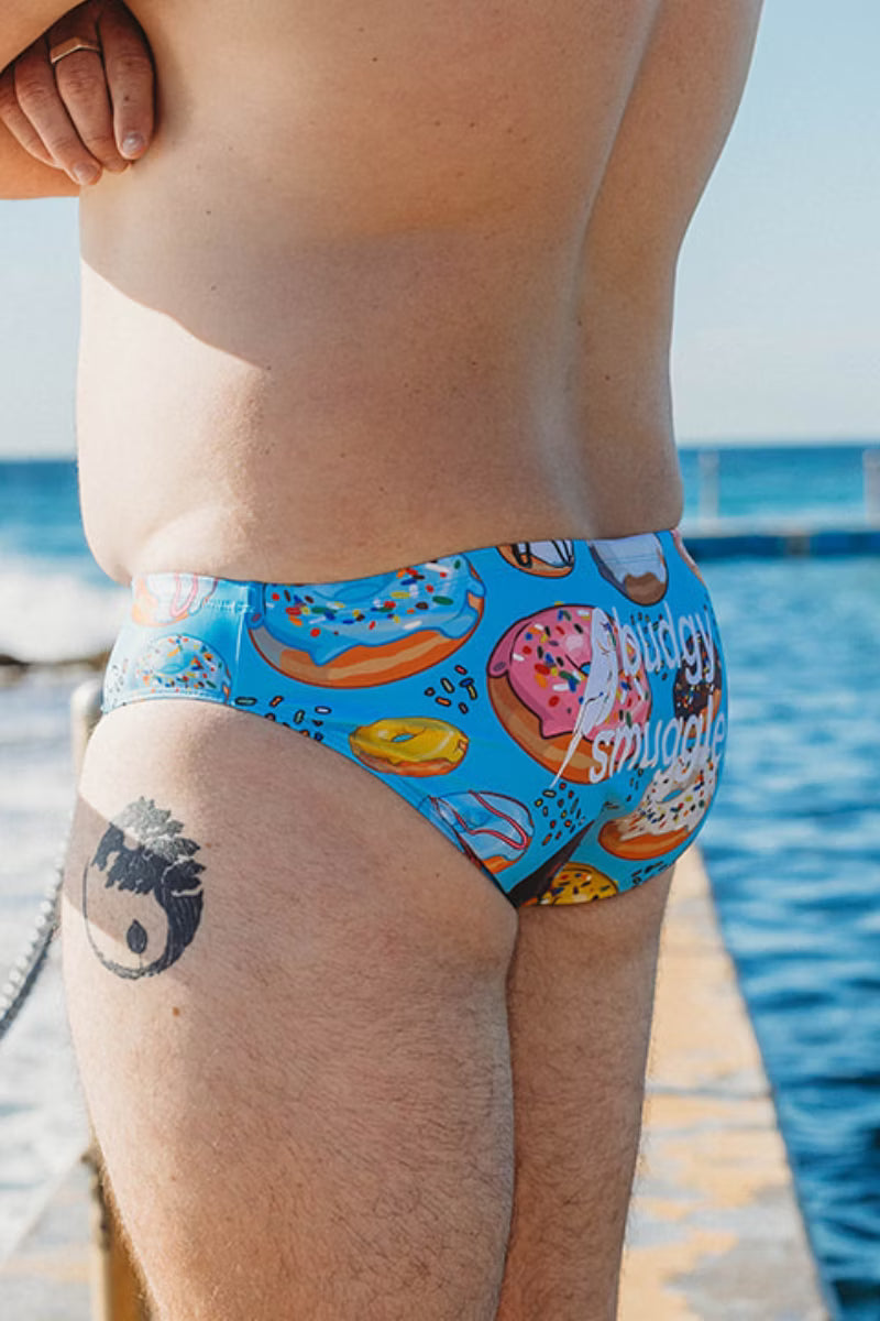 Side view of Donuts men's swimmers with pink, chocolate and sprinkle donuts on blue